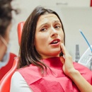 A woman sitting in the dentist’s chair holding her cheek in pain and talking to the dentist