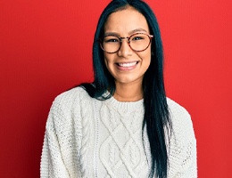 A young woman with long, dark hair and wearing glasses and a cream sweater, smiling after receiving cosmetic teeth bonding in Castle Rock
