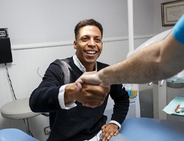 A young man wearing a black sweater shakes hands with a dentist during an initial consultation