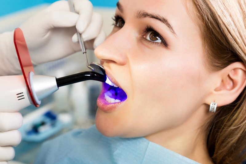 a dentist using a curing light to harden the resin used for cosmetic bonding on a female patient’s smile