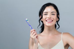 a young woman with dark hair holding a manual toothbrush and smiling