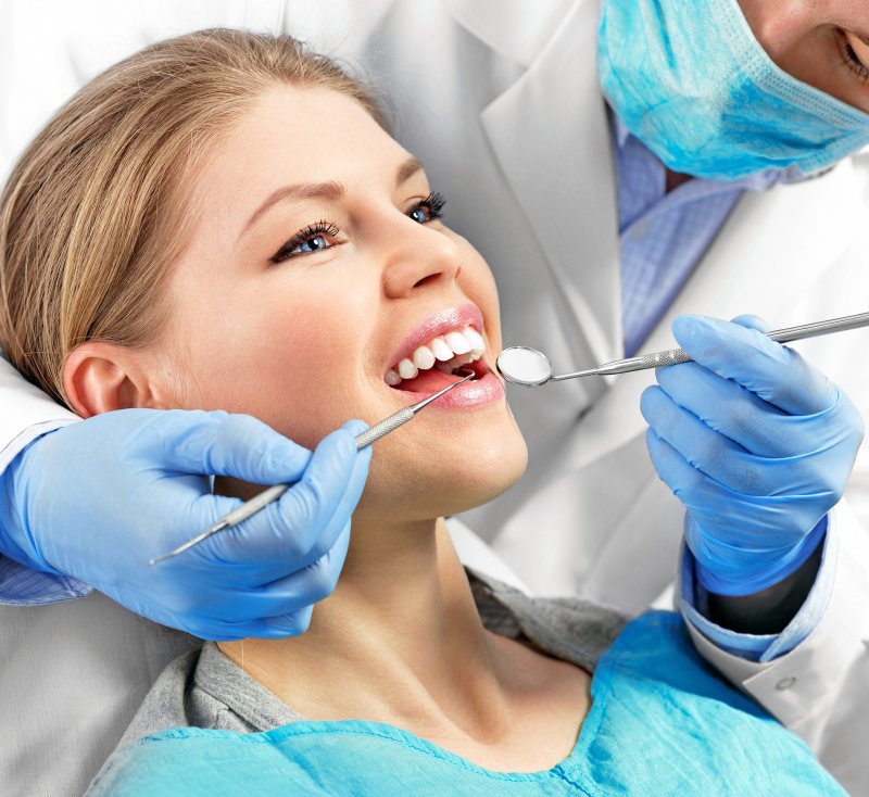 a young woman having a dentist examine her smile before removing her metal crown in Castle Rock